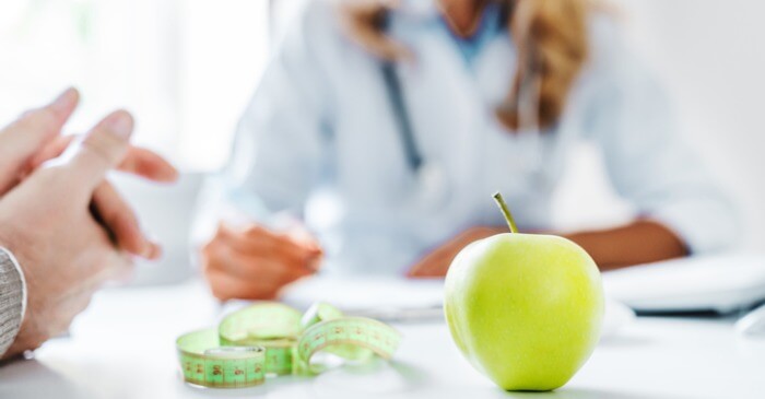 Kunde sitzt beim Ernährungscoach für eine Ernährungsberatung und auf dem Tisch liegen ein grüner Apfel sowie ein Maßband